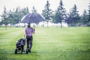 Mann geht im Regen über den Golfplatz