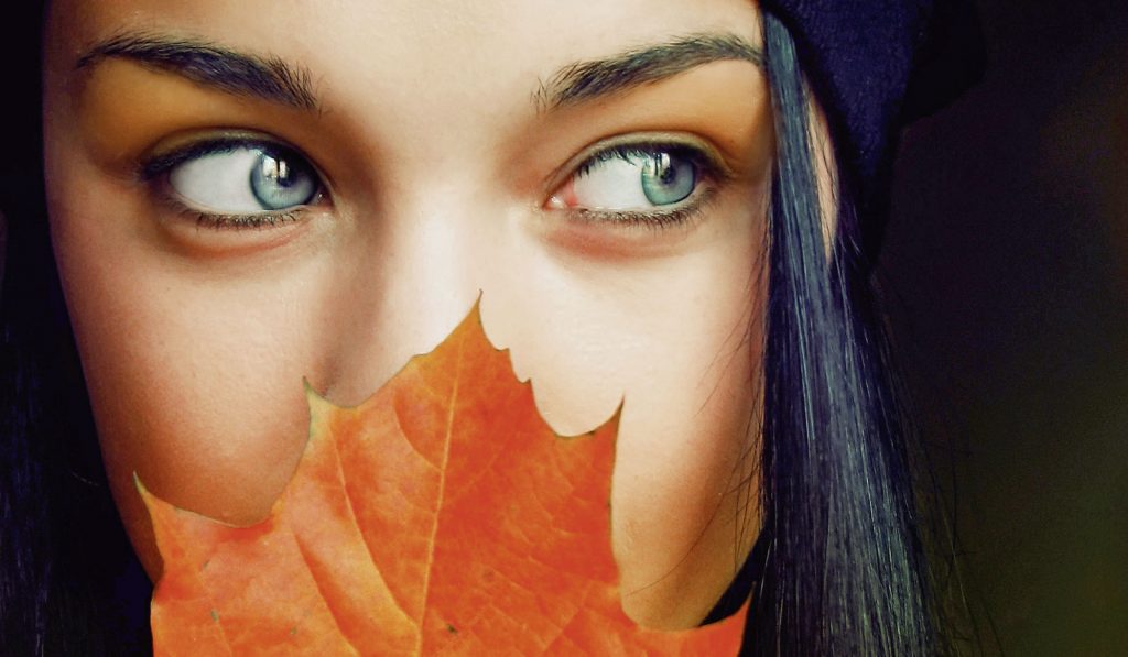Frau mit Herbstblatt vor dem Gesicht