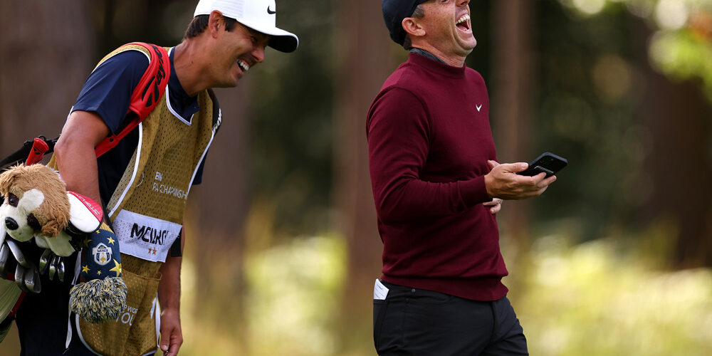 Rory McIlroy lacht mit einem Handy in der Hand.