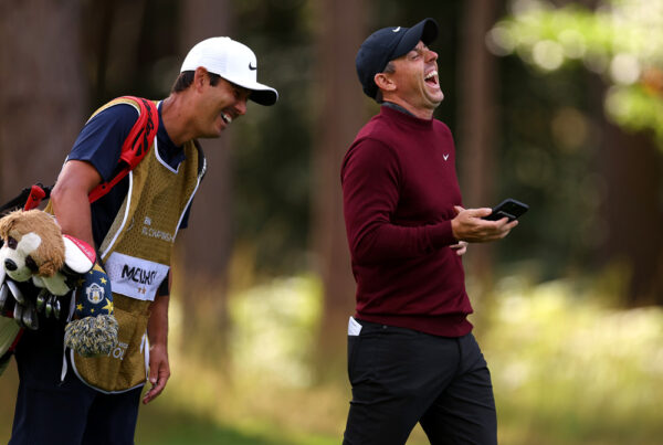 Rory McIlroy lacht mit einem Handy in der Hand.